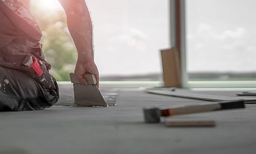 Arbeiter kniet auf dem Boden mit Werkzeugen in der Hand