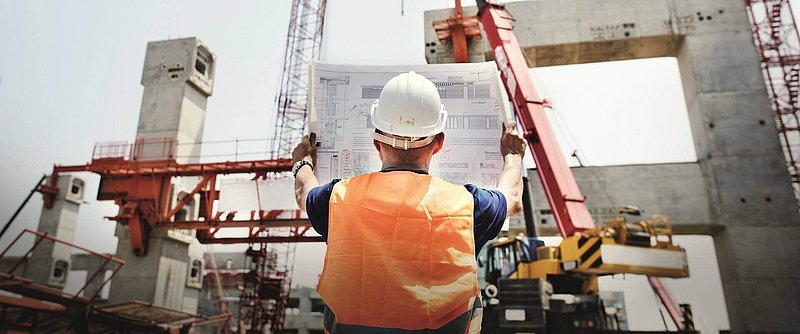 Baumeister mit Helm auf einer Baustelle mit Kran